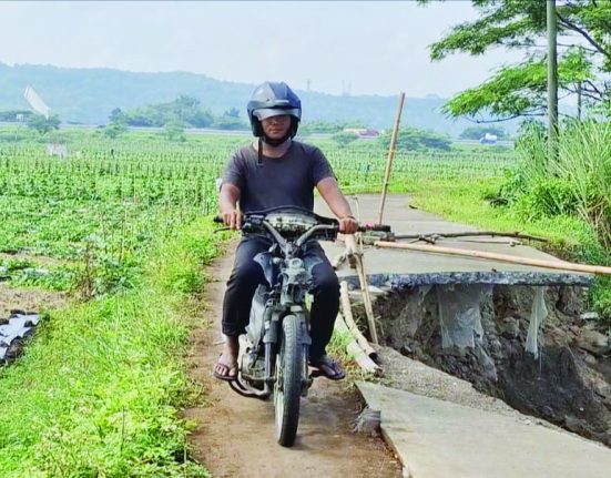 Salah seorang pengendara motor sedang melewati jalan penghubung Dusun Sudimoro, Desa Kertomulyo dengan Dusun Weleng, Desa Tunggulsari di Kecamatan Brangsong, Kendal yang ambrol dan terkikis aliran air Sungai Blorong. (Arvian Maulana | Mantranews.id)