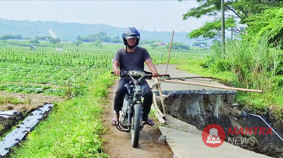Salah seorang pengendara motor sedang melewati jalan penghubung Dusun Sudimoro, Desa Kertomulyo dengan Dusun Weleng, Desa Tunggulsari di Kecamatan Brangsong, Kendal yang ambrol dan terkikis aliran air Sungai Blorong. (Arvian Maulana | Mantranews.id)